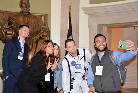 Practitioners, residents, fellows, and postgraduate students smiling for a photo in front of a statue in APhA headquarters